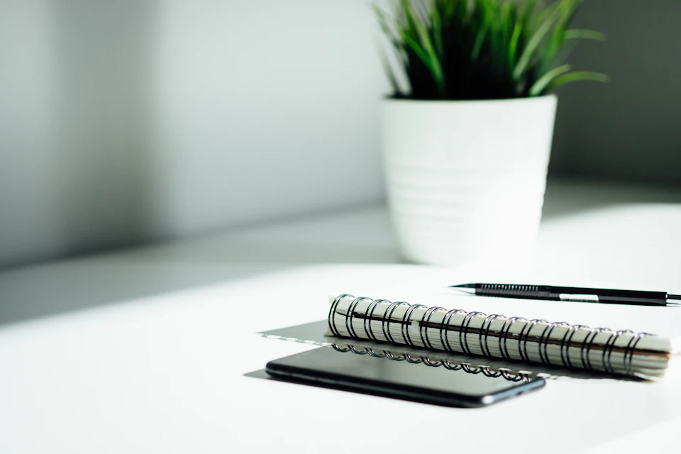 Caneta, caderno e telemóvel em cima de uma mesa