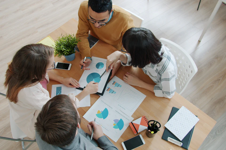 Equipa a trabalhar em conjunto à volta de uma mesa com gráficos